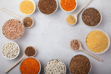 white beans, peas, lentils, buckwheat, corn grits cups and wooden spoons on a white background. superfood