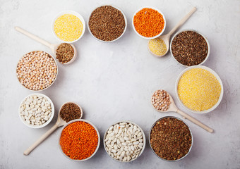 white beans, peas, lentils, buckwheat, corn grits cups and wooden spoons on a white background. superfood