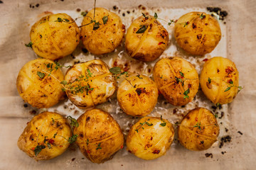 A horizontal top view artificial light photo of baked baby potatoes with salt, pepper, olive oil and thyme, in a glassware on a linen towel.