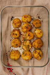 A vertical top view artificial light photo of baked baby potatoes with salt, pepper, olive oil and thyme, in a glassware on a linen towel.