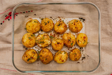 A horizontal top view artificial light photo of baked baby potatoes with salt, pepper, olive oil and thyme, in a glassware on a linen towel.