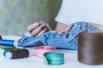 women's hands, a tailor sews clothes at a table on which spools of thread lie