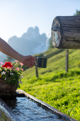 Naklejka na ściany i meble Close up shot of the tourist hand holding a green mug at a mountain spring. Hiking concept