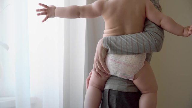 Young mother holding her baby in the bedroom newar the window. Diaper