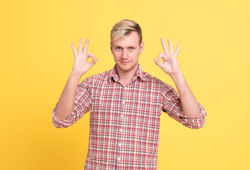 Portrait of a cheerful young man showing okay gesture looking at excellent isolated on the yellow background.