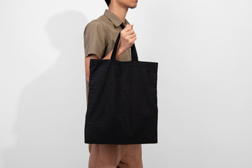 Man is holding black bag canvas fabric for mockup blank template isolated on gray background.