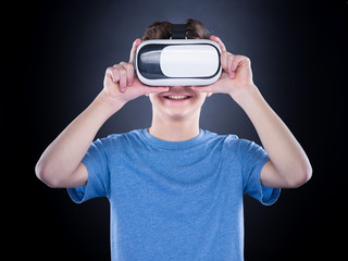 Happy teen boy wearing virtual reality goggles watching movies or playing video games. Cheerful smiling teenager looking in VR glasses. Funny child experiencing 3D gadget technology.