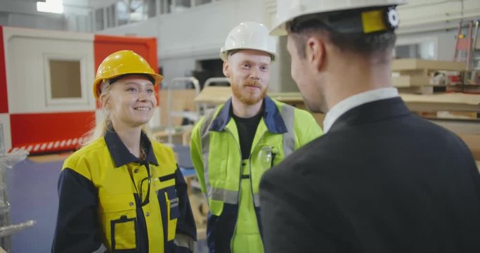 Portrait of factory workers giving high five while talking to manager in workshop of modern plant