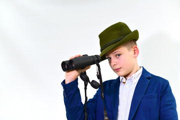 Portrait of confident teenager in formalwear with huntsman's hat and binoculars over white isolated grey background looking into the camera.