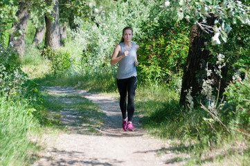 Beautiful, athletic, slim woman with headphones running through the park in the summer sunny morning. Morning jogging and sports
