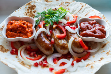 Fried pork sausages on pita bread with ketchup and Armenian appetizer Aivar with vegetables. Lavash, red bell pepper, onions, sausages. Oktoberfest food, the concept of the pub