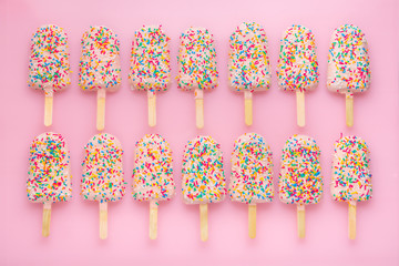rows of popsicles with covered icing and sprinkles on pink background