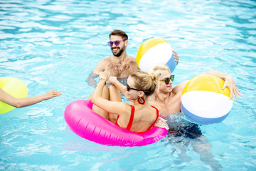 Group of a happy friends having fun, swimming with inflatable toys in the swimming pool outdoors during the summertime