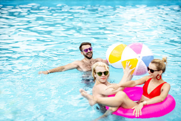 Group of a happy friends having fun, swimming with inflatable toys in the swimming pool outdoors during the summertime