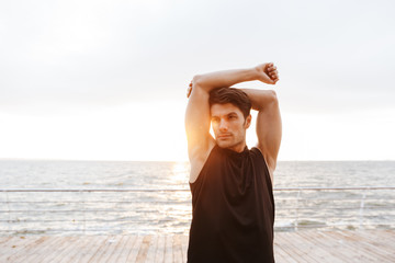 Photo handsome man in tracksuit doing exercise while working out on wooden pier at seaside