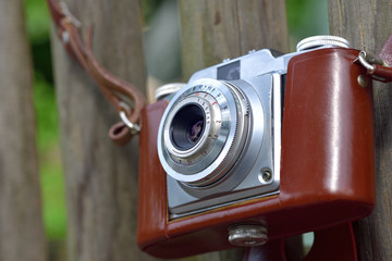 Nahaufnahme einer alten analogen Fotokamera mit Lederhülle an einem Gartenzaun hängend