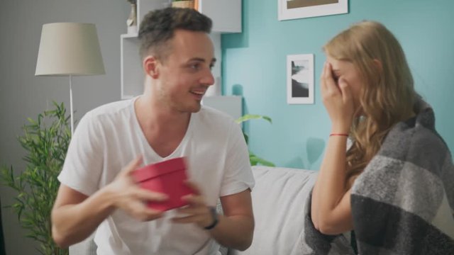 Young man gives a gift to a happy girlfriend in the morning in the living room