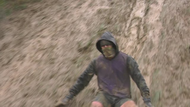 An obstacle course racer slides down a muddy hill