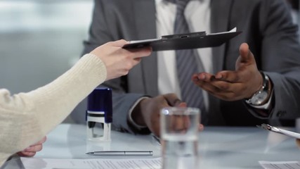 Tracking hands shot of unrecognizable Caucasian man and woman concluding contract in notary office and handing over their signed copies to dark-skinned professional man in business suit and tie