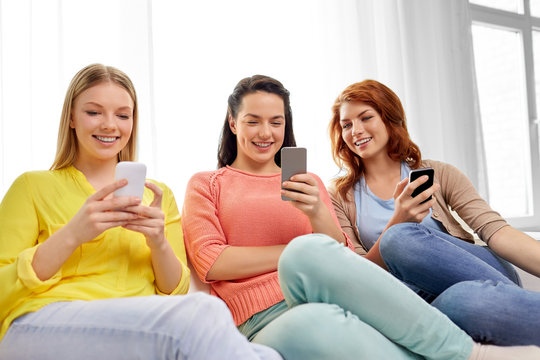 friendship, technology and internet concept - three smiling teenage girls or friends with smartphones at home