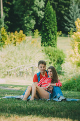 young loving couple is sitting on a plaid in the park, hugging, fooling around and enjoying nature. Picnic for couples in love.