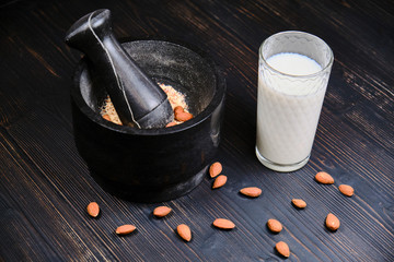 Grind almonds to make milk. A glass of milk and almonds on a wooden table. Mortar with crushed nuts on a dark wooden background