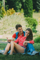 young loving couple is sitting on a plaid in the park, hugging, fooling around and enjoying nature. Picnic for couples in love.