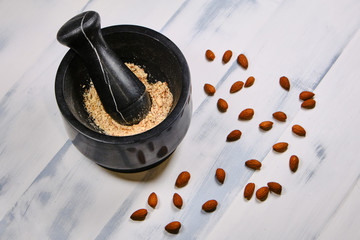 Fototapeta premium Almonds for cooking on a wooden white background. Grinding nuts in a mortar. Preparation of almond flour, top view.