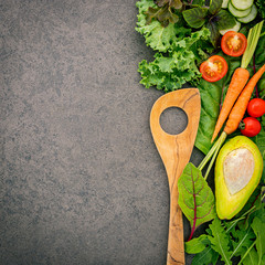 Wooden spoon and vegetables on dark stone background. Healthy food and cooking concept.