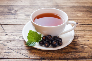 Cup of tea and fresh blackcurrant berries on a wooden background. Copy space.