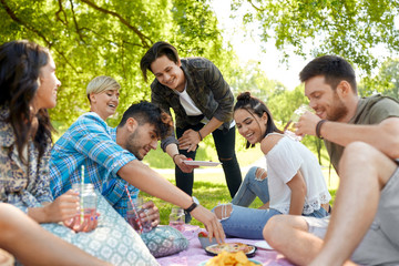 friendship and leisure concept - group of happy friends with non alcoholic drinks and food at picnic in summer park