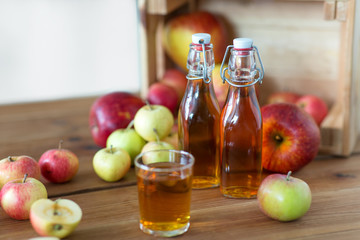 fruits, food and harvest concept - glass and bottles of apple juice or cider on wooden table