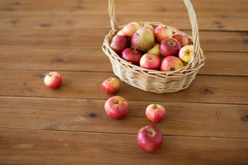 fruits, food and harvest concept - ripe apples in wicker basket on wooden table