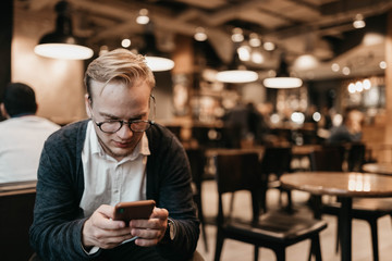european male businessman with glasses uses a smartphone in a coworking cafe with a warm cozy light