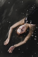 Young woman with raised arms in the water. Black water. Vertical photo