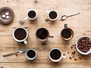 Verschiedene Kaffeetassen und eine Schüssel mit gerösteten Kaffeebohnen auf einem Holztisch, Flat lay