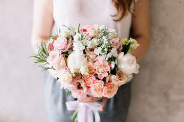 very nice young woman holding a beautiful blossoming flower wedding bouquet of fresh peony, roses, carnations, eustoma, eucalyptus in tender pastel pink colors on the grey wall background