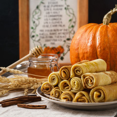 Stack of pumpkin crepes with honey and cinnamon on a table.