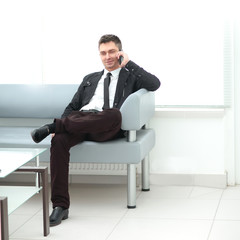 businessman sits in the lobby of the office and talking on a smartphone