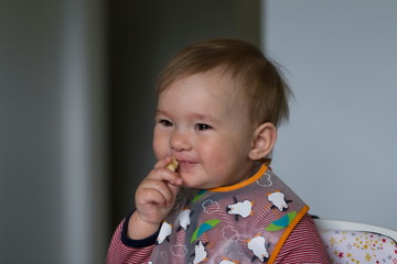 Closeup of cute fair smiling toddler girl eating a piece of banana while sitting in her high chair...