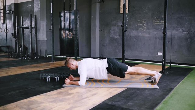 Athletic strong man does plank saws as part of his cross fitness, bodybuilding gym training routine. Intermediate no equipment exersize to endurance for abs and core. Calisthenics and morning