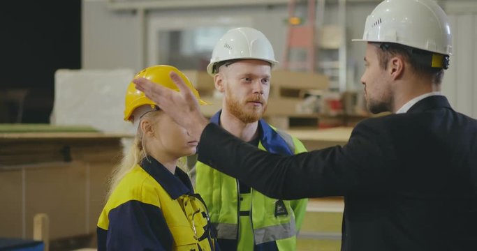 Serious strict young manager scolding two factory workers