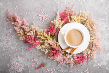 Fototapeta na wymiar Pink and red astilbe flowers and a cup of coffee on a gray concrete background. top view.