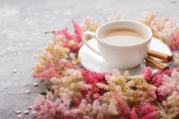 Pink and red astilbe flowers and a cup of coffee on a gray concrete background. side view.