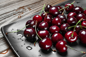 Ripe juicy sweet cherries in a black plate on a wooden background. Top view wet fresh cherries with...