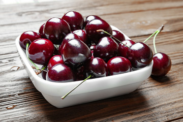 Fresh ripe juicy sweet cherries in a white plate on a wooden background.