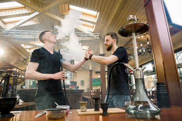 Hookah in the process preparation in cozy hookah bar. Two young men shisha masters giving five while preparing hookah for smoking