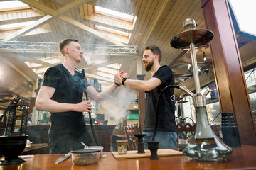 Hookah in the process preparation in cozy hookah bar. Two young men shisha masters giving five while preparing hookah for smoking