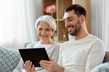 family, generation and technology concept - happy smiling senior mother and adult son with tablet computer at home