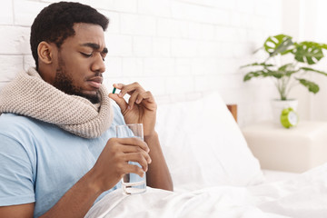 African-american man holding glass of water and looking at pill